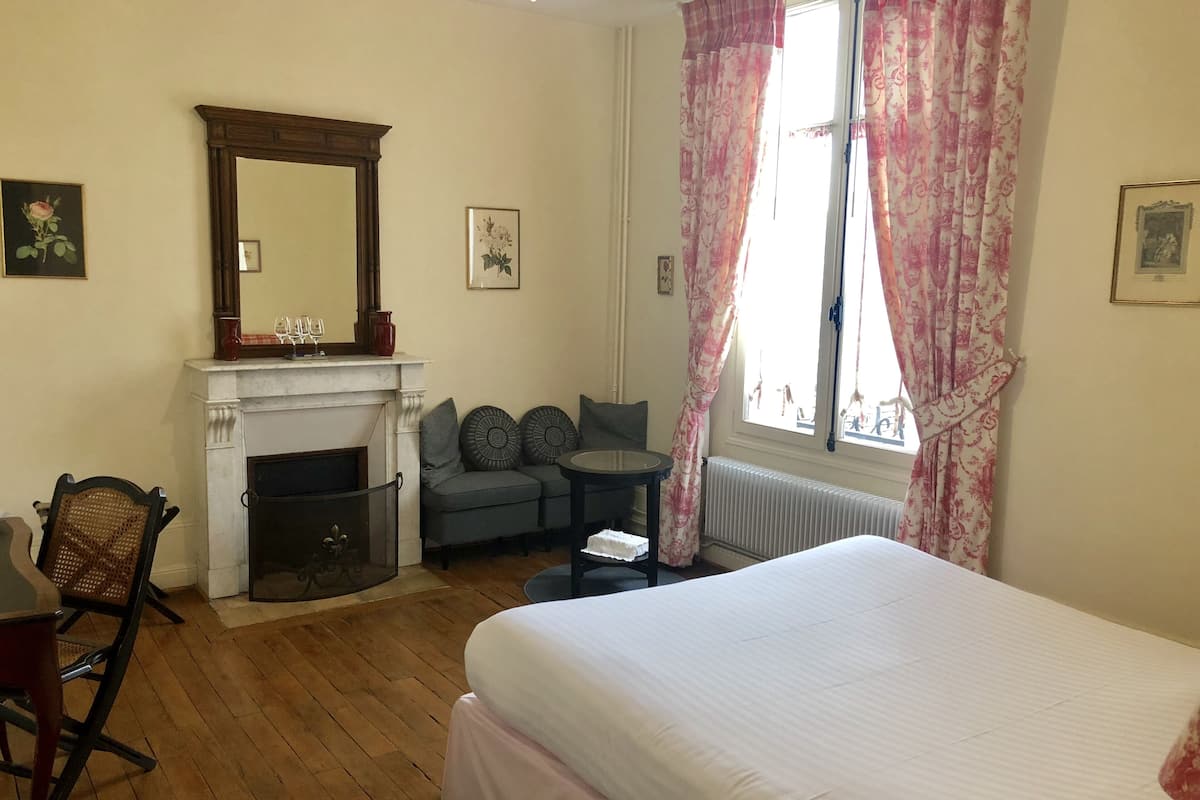 A bedroom with a bed, a fireplace, a desk, and a window with curtains.