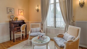 A cozy room with a piano, two armchairs, a round table with a tray of items, and a window with curtains. - Manoir Du Parc - Adults Only (Amboise)