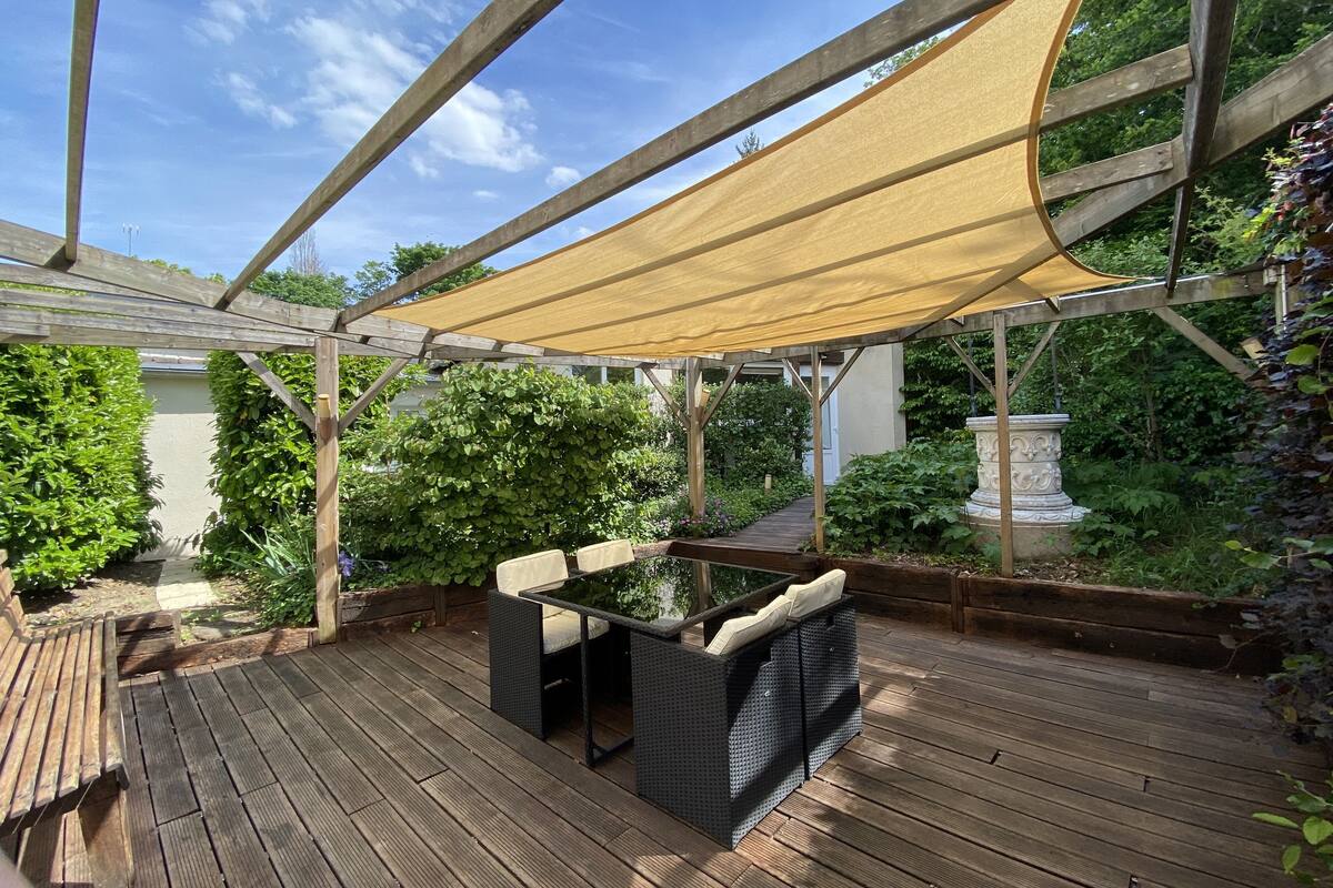 A wooden deck with a pergola and a table with cushions.