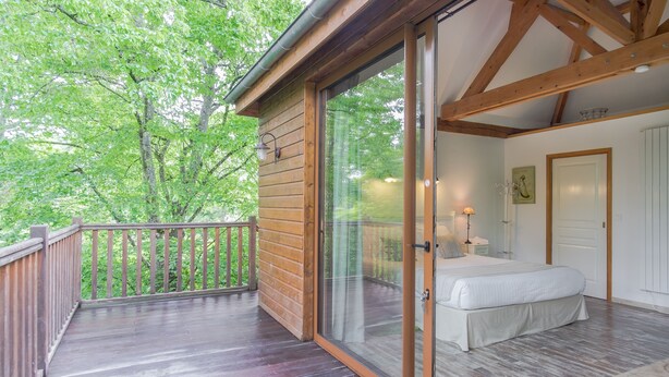 A bedroom with a large sliding glass door leading to a balcony, wooden deck, and a view of trees. - Manoir Du Parc - Adults Only (Amboise)