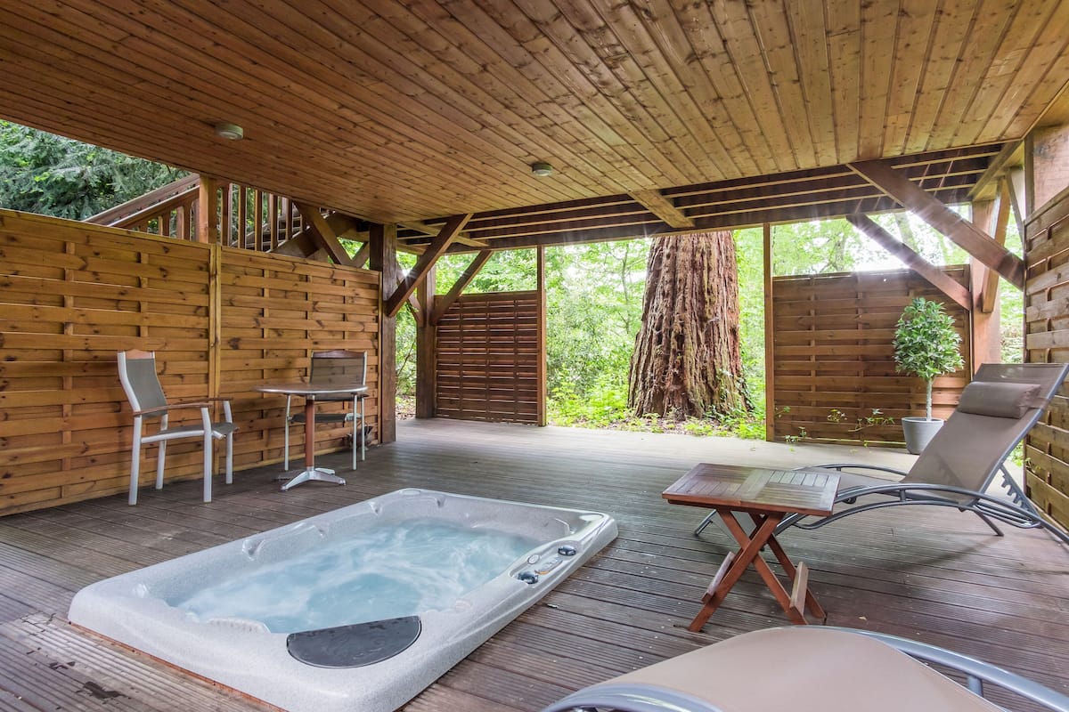 A wooden deck with a hot tub, lounge chairs, and a table.