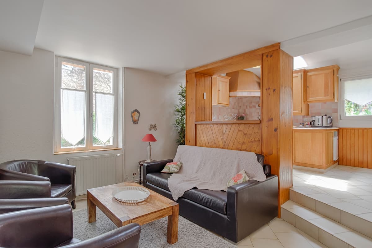 A compact living space with a sofa, a coffee table, and a kitchen area with wooden cabinets and a window.