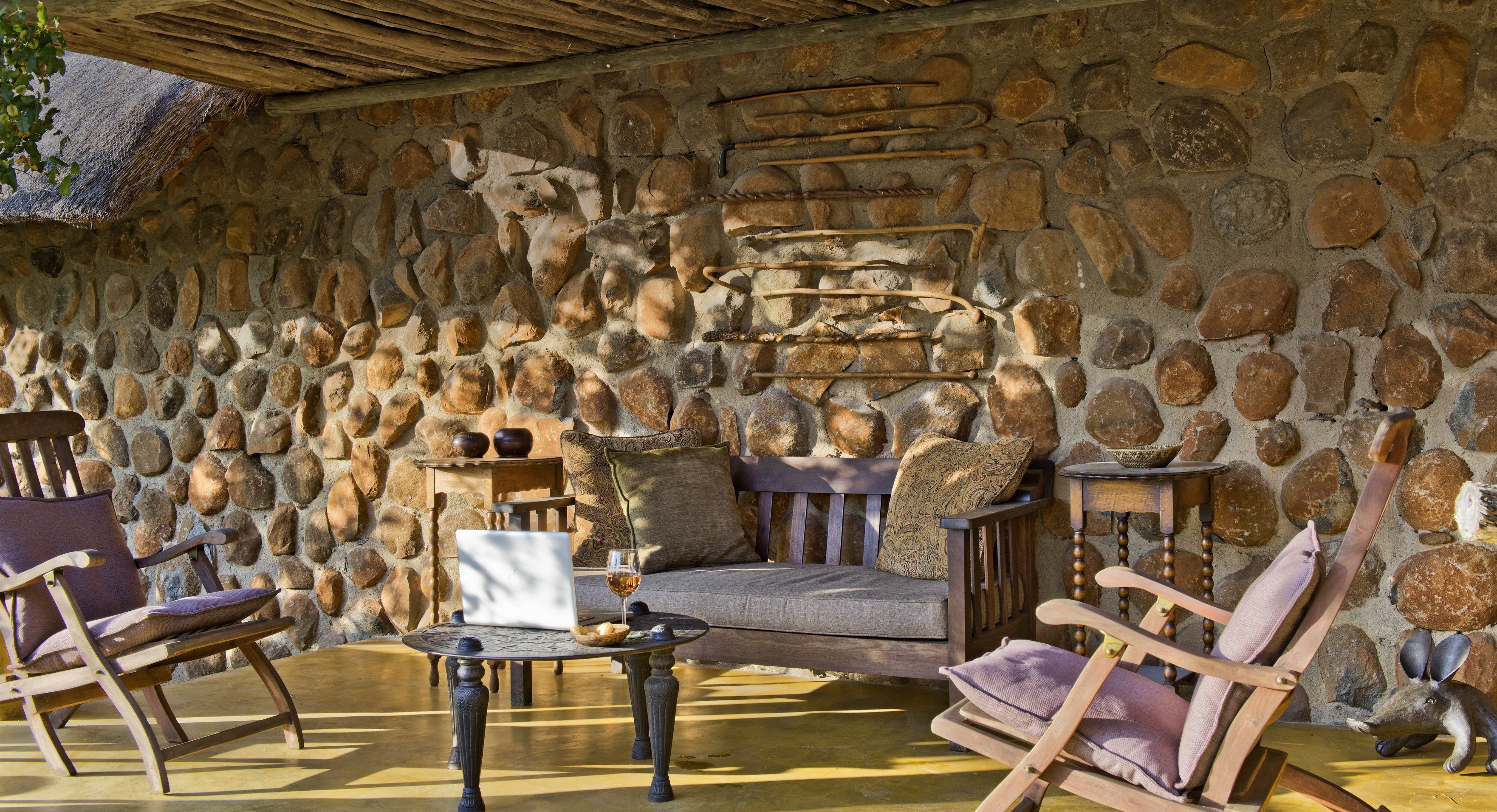 Une pièce aux murs de pierre, avec un banc en bois, une table sur laquelle se trouvent un ordinateur portable et un verre, ainsi qu’une petite figurine d’animal.