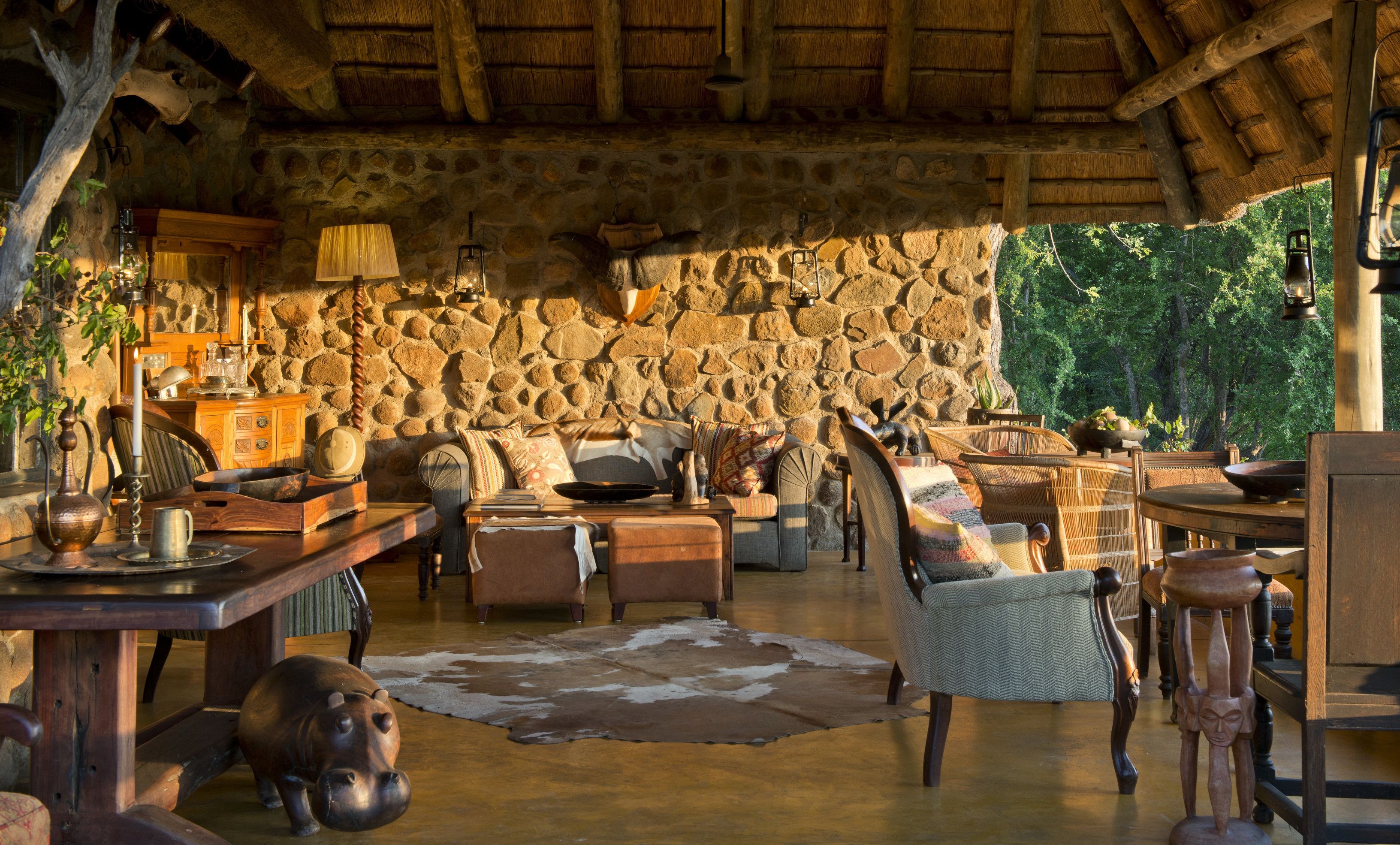 A rustic interior with stone walls, wooden furniture, and a thatched roof.