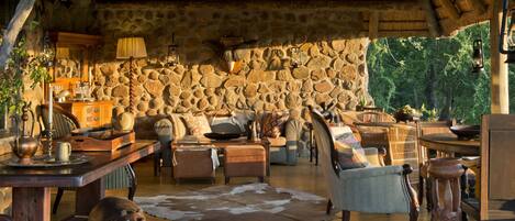 A rustic interior with stone walls, wooden furniture, and a thatched roof.