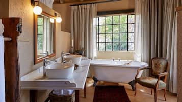 Une salle de bain avec une grande baignoire, deux lavabos, une chaise et une fenêtre avec des rideaux.