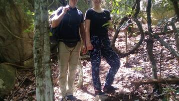 Two people walking on a forest trail surrounded by trees and rocks.