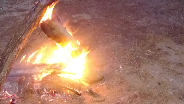 A campfire with two people seated on chairs in a natural setting. - go camping (Ella)