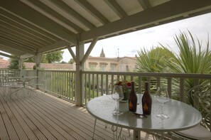 A covered outdoor area with a round table, two wine glasses, and bottles, surrounded by metal chairs and a railing. - Logis Hôtel l'Essille (Bassac)