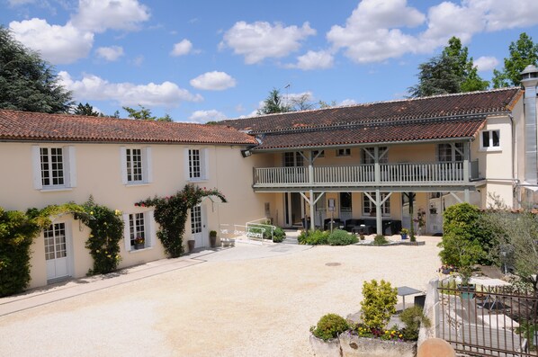 A traditional building with a tiled roof, a covered porch, and a gravel courtyard. - Logis Hôtel l'Essille (Bassac)
