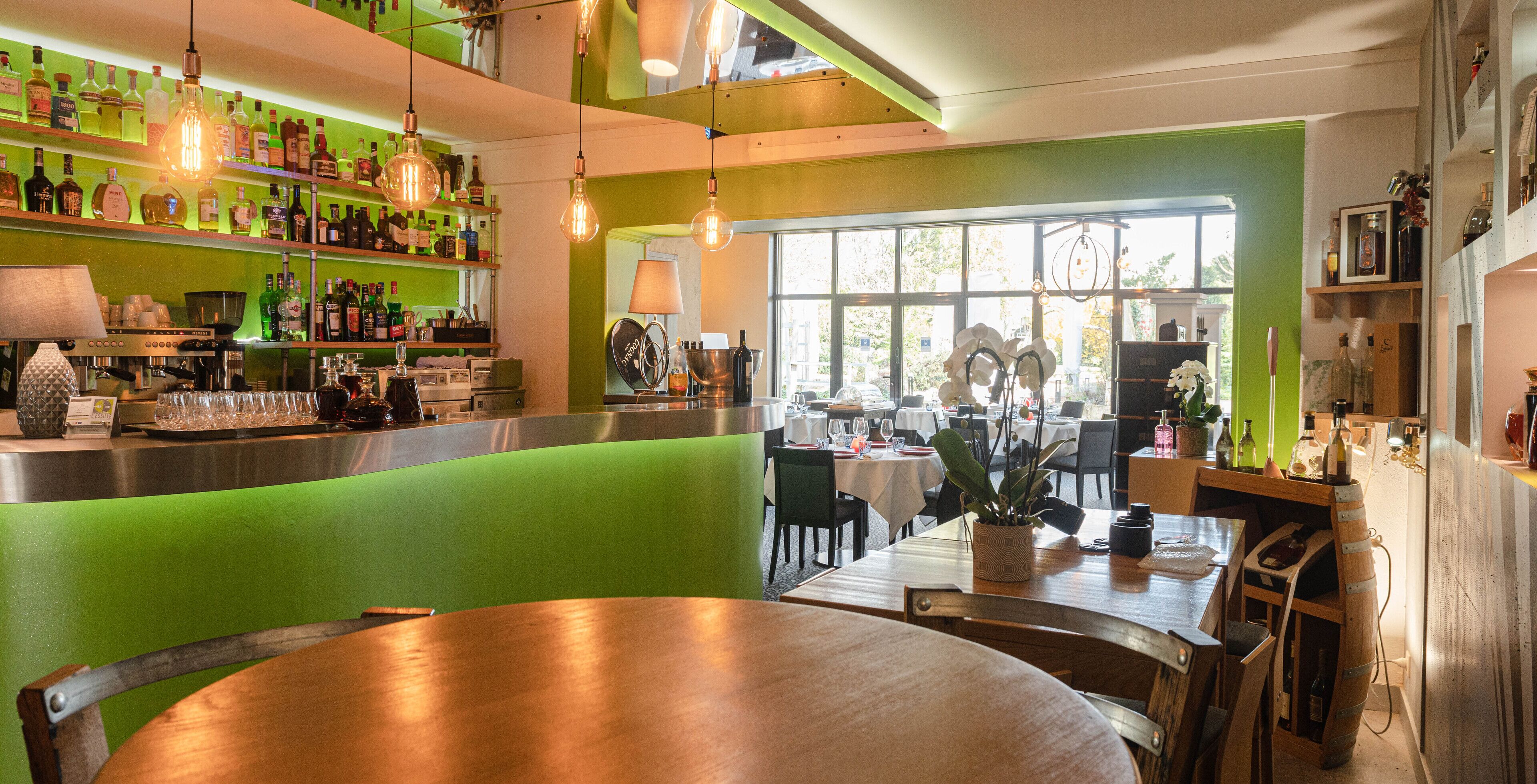 A restaurant with green booths, a bar area with bottles, and a view of the outdoors.