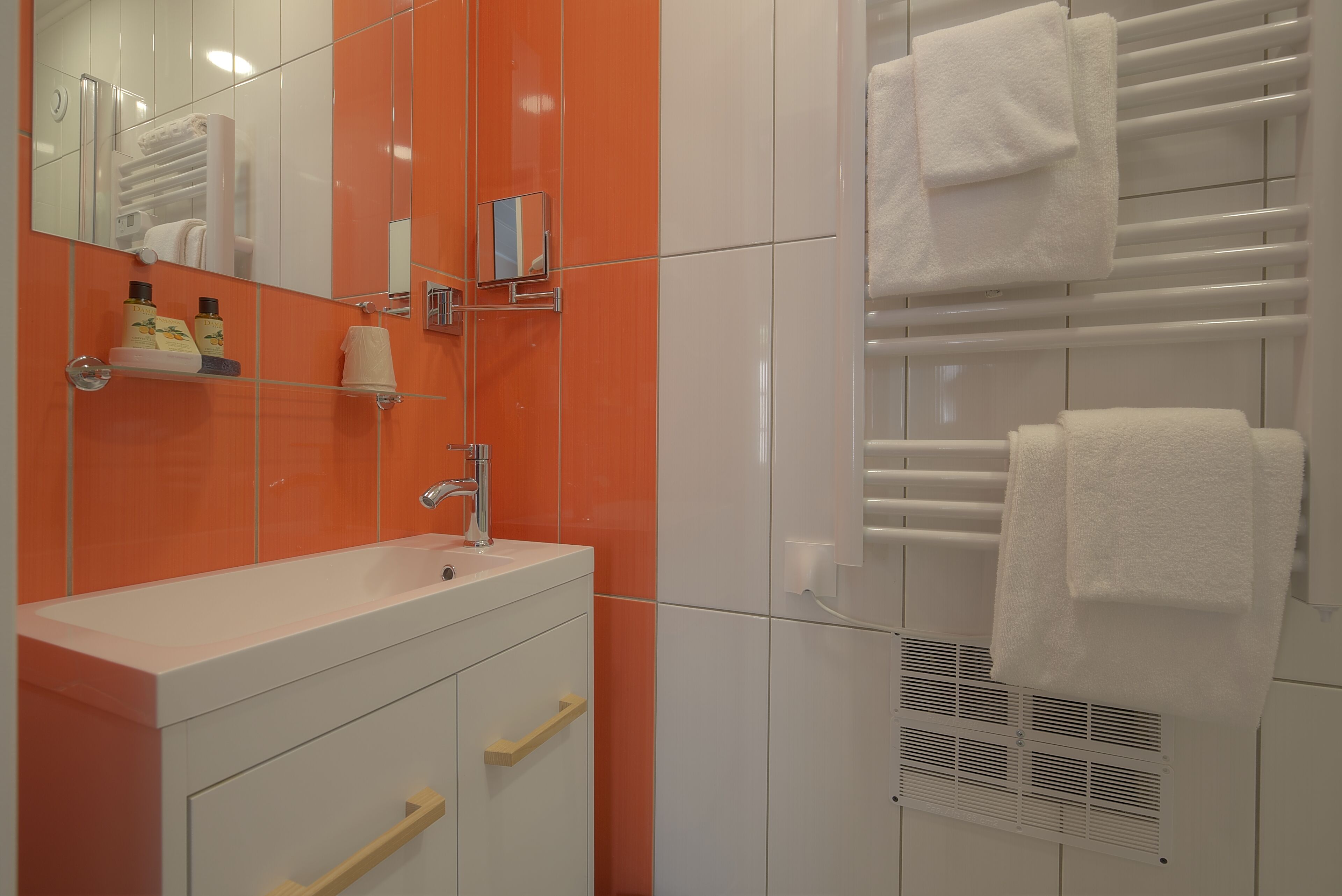 A bathroom with a white sink, orange tiles, a mirror, and a towel rack.