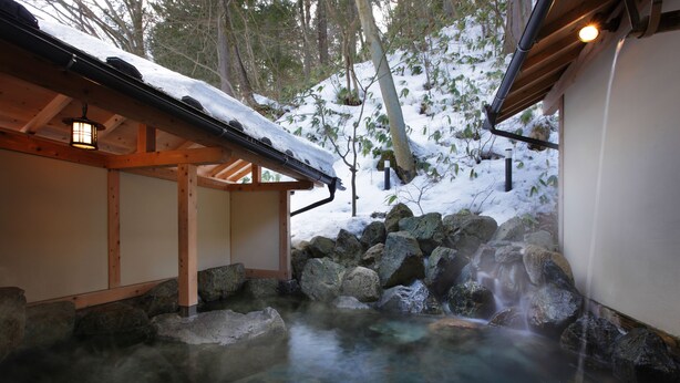 A traditional wooden structure with a snow-covered roof, a stone water feature, and a wooden walkway. - Yama no Yado Shimofujiya (Nasushiobara)