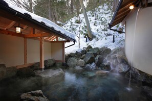 Una estructura de madera tradicional con techo nevado, una fuente de piedra y un pasillo de madera.