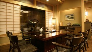 A traditional Japanese-style dining room with a low table surrounded by chairs, a wooden floor, and a sliding door with a view of a garden. - Yama no Yado Shimofujiya (Nasushiobara)