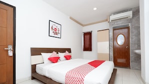 Una camera d'albergo con un letto, una testiera in legno, un quadro appeso al muro, una finestra con tende, una porta e un condizionatore d'aria.