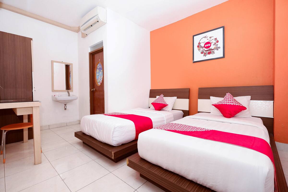 A hotel room with two beds, a desk, a chair, a sink, and an air conditioning unit.