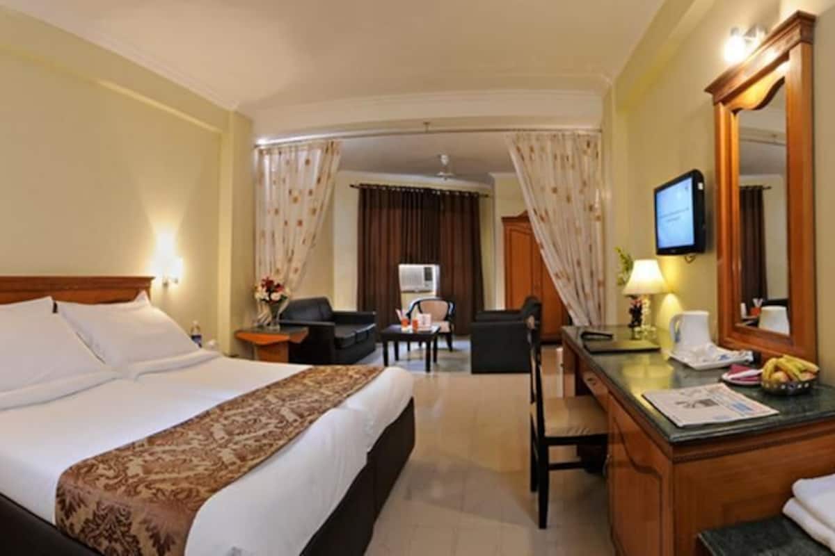 Habitación de hotel con una cama grande, un escritorio, una silla, un espejo y un televisor.