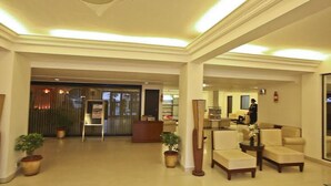 Una hall d'albergo con reception, zona salotto e piante in vaso.