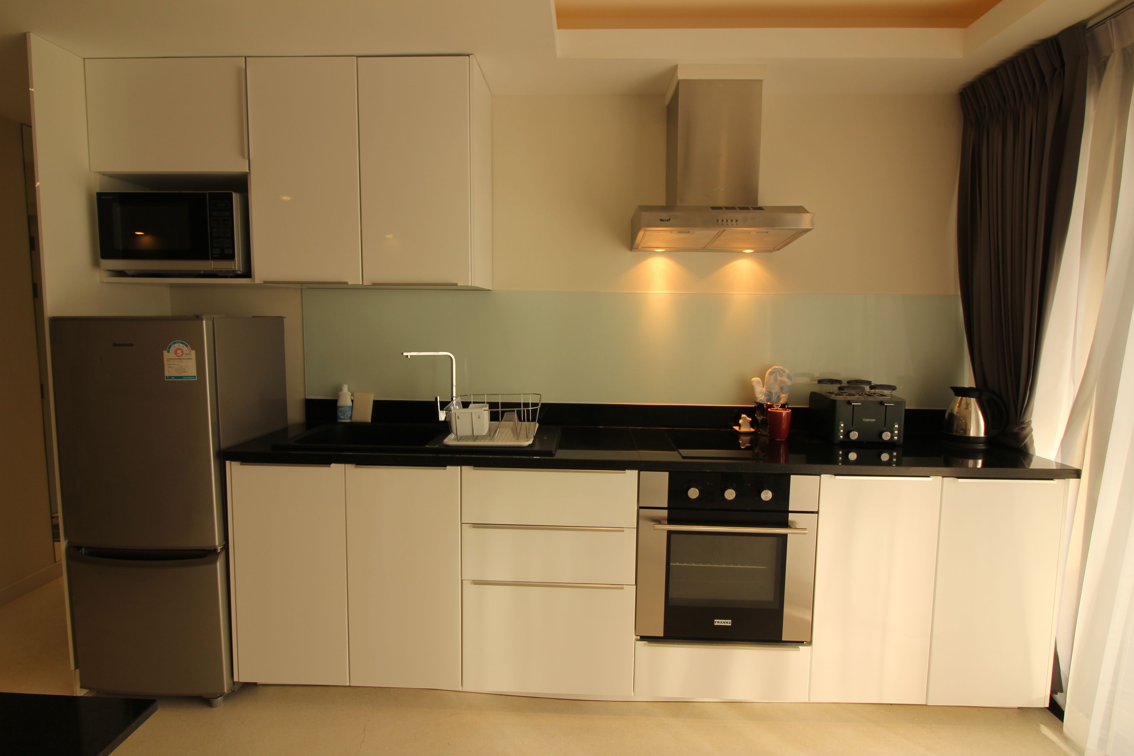 A modern kitchen with a stainless steel refrigerator, oven, and microwave. It includes white cabinets, a black countertop, and a stainless steel range hood.