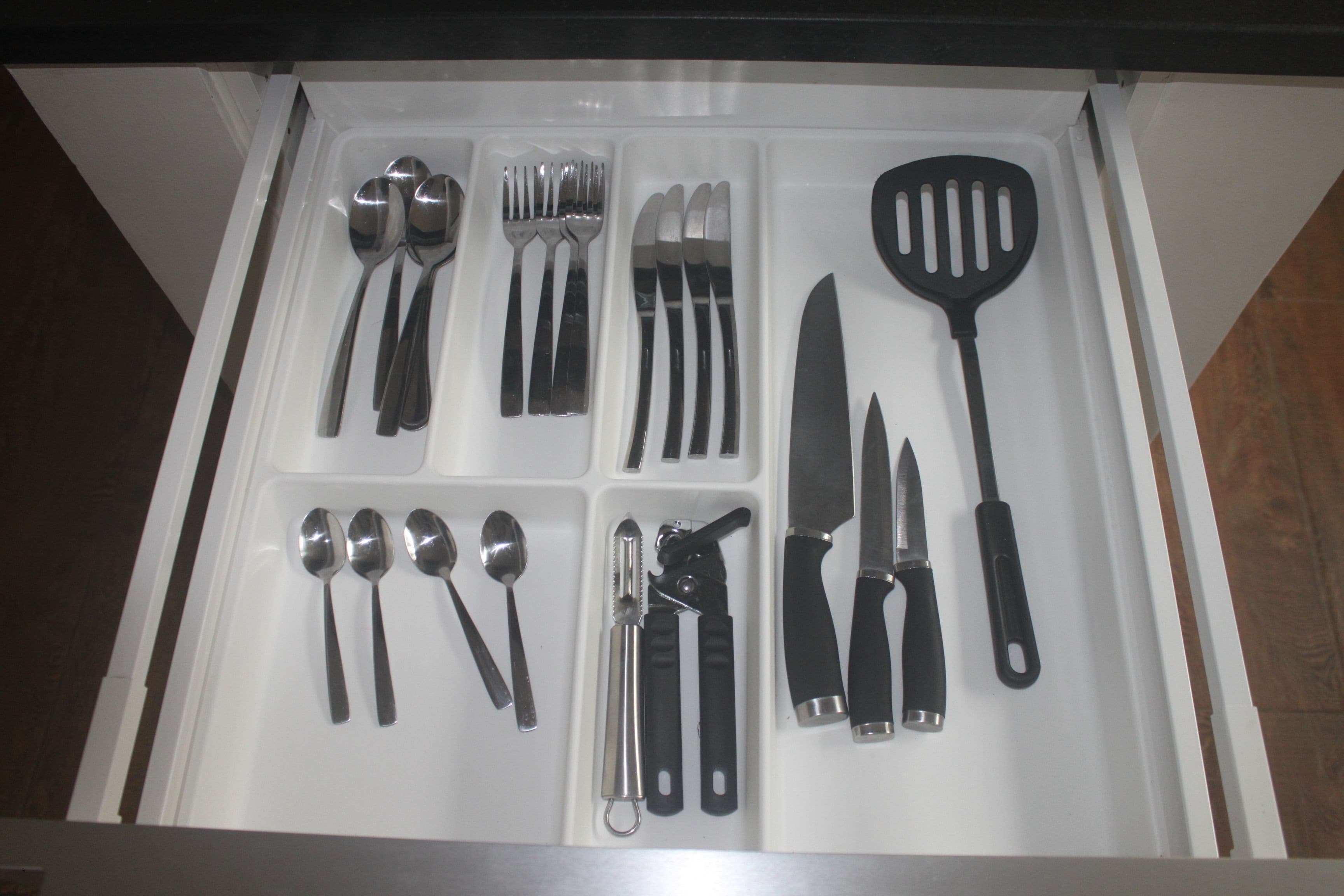 Un cajón con diversos utensilios de cocina, incluyendo cucharas, tenedores, cuchillos y una espátula.
