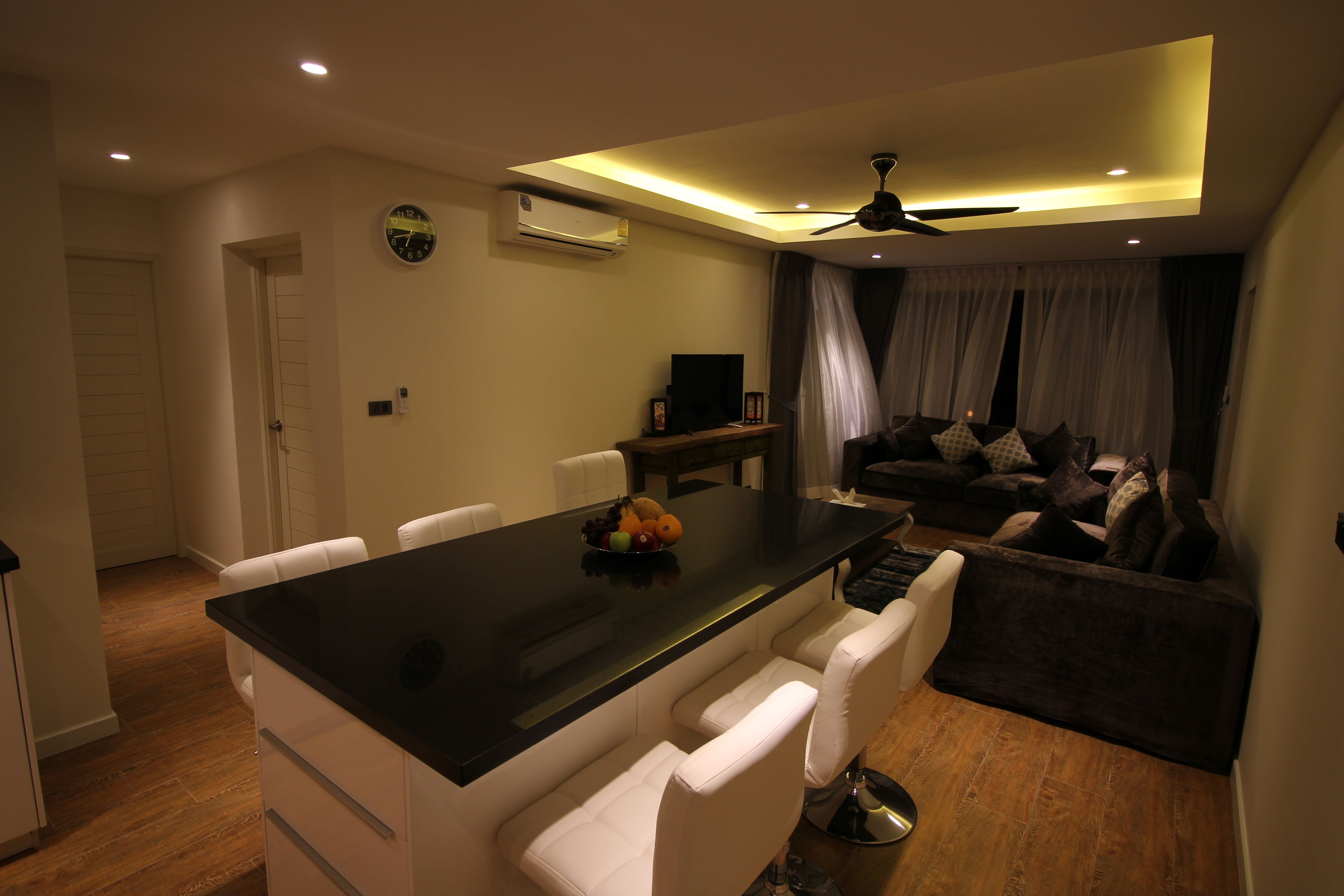 A modern dining area with a black table, white chairs, a ceiling fan, and a living area with a sofa and curtains.