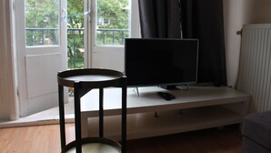 A room with a television on a stand, a small table, and a window with curtains. - MyCityLofts - Aelbrechtskade (Rotterdam)