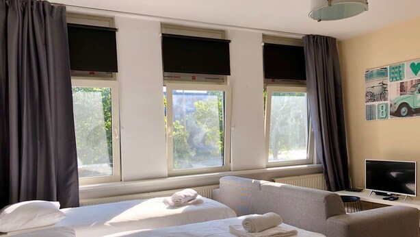 A hotel room with two beds, a sofa, a TV, and large windows with curtains. - MyCityLofts - Aelbrechtskade (Rotterdam)