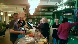 A bar area with a counter, a glass display case with a cake, and shelves stocked with bottles. - Lækur Hostel (Reykjavik)