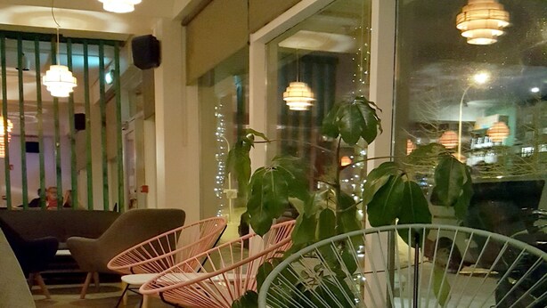 A dining area with a table, chairs, and a glass of wine. There are potted plants and a view of the street outside. - Lækur Hostel (Reykjavik)