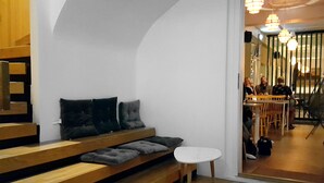 A modern interior with a wooden staircase, a sofa with cushions, a small white table, and a dining area with people. - Lækur Hostel (Reykjavik)