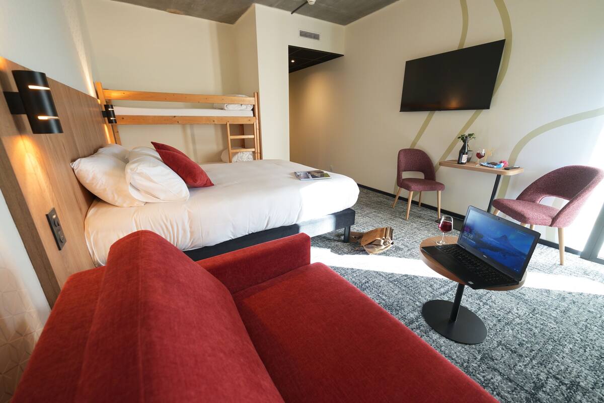 A hotel room with a bunk bed, a desk with a laptop, a chair, and a TV on the wall.