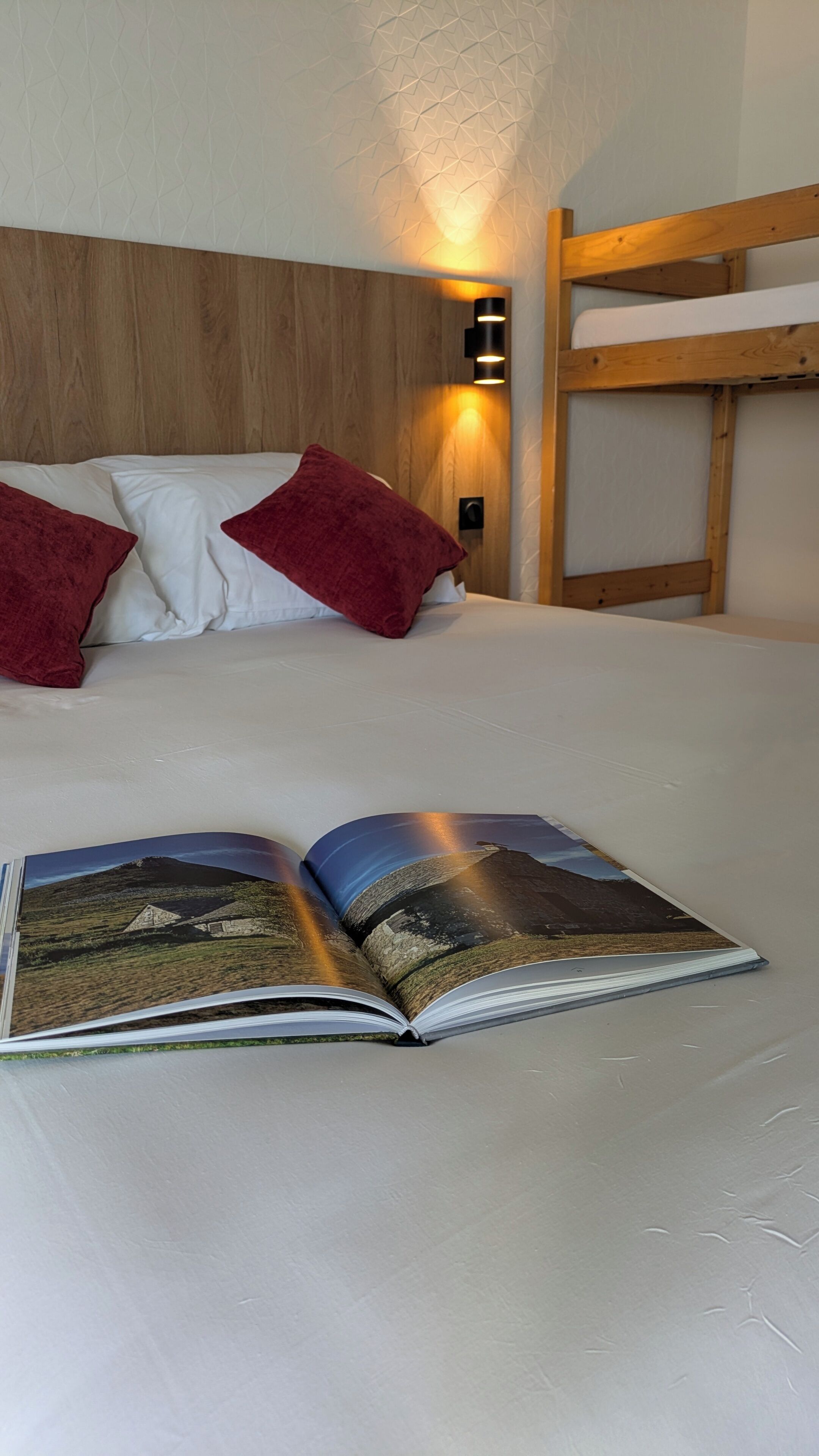 Una cama con cabecera de madera, almohadas rojas y un libro abierto sobre la colcha.