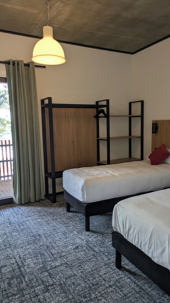 A room with two beds, a hanging light fixture, a wooden wardrobe, and a view of the outdoors.