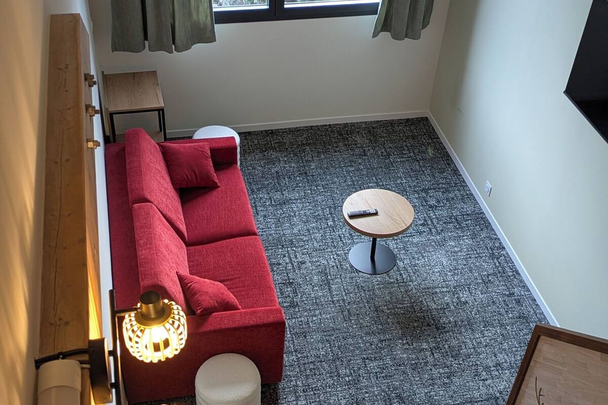 A room with a red sofa, a small round table, a lamp, and a painting on the wall.