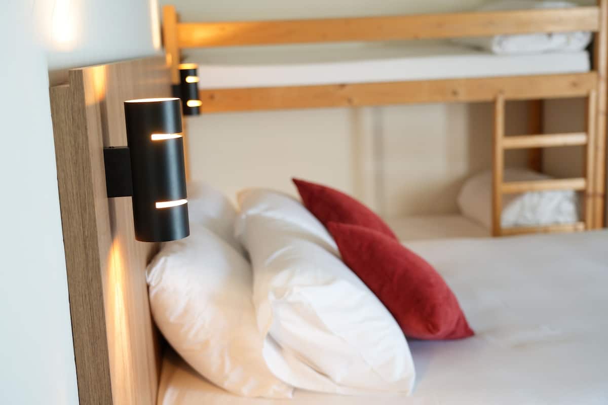 A bunk bed with white and red pillows, a wooden headboard, and a wall-mounted light fixture.
