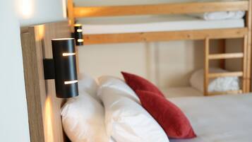 Een stapelbed met witte en rode kussens, een houten hoofdbord en een wandlamp.