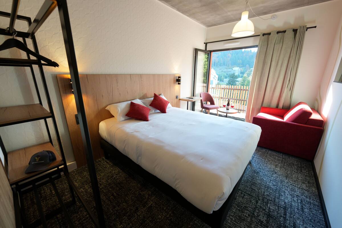 A hotel room with a large bed, a desk, a chair, and a view of the outdoors.
