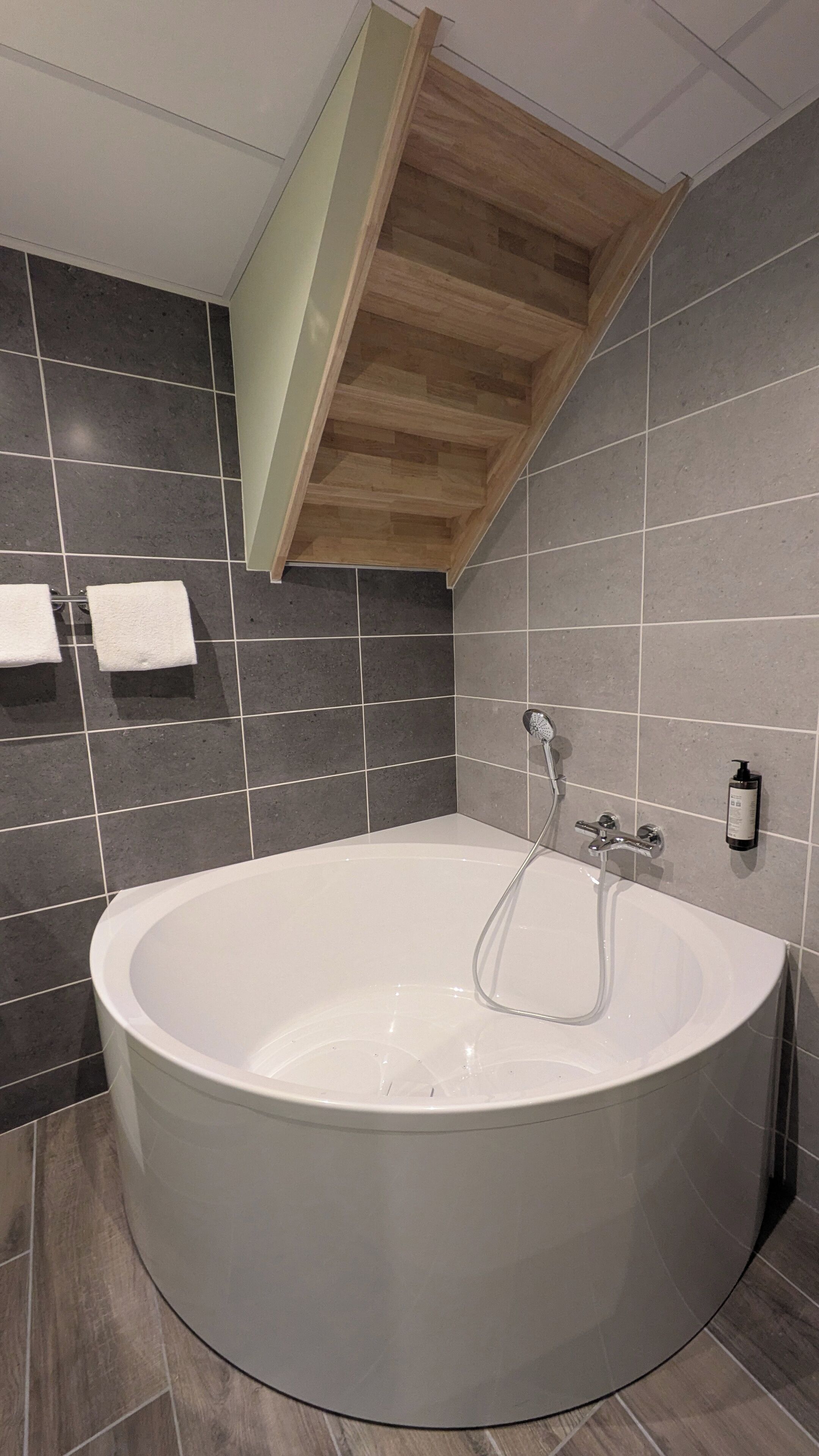 A modern bathroom with a freestanding bathtub, dark tiled walls, and a wooden ceiling.