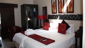 A hotel room with a large bed, a red chair, a desk with a lamp, and artwork on the wall. - African Tribes Guest Lodge & Conference (Kempton Park)