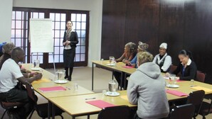 A conference room with a presentation setup, including a speaker at the front and attendees seated at tables with notebooks and water bottles. - African Tribes Guest Lodge & Conference (Kempton Park)