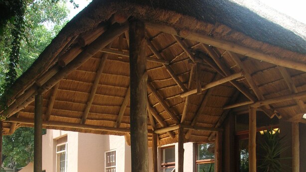 A wooden pavilion with a thatched roof, surrounded by potted plants and a flower bed. - African Tribes Guest Lodge & Conference (Kempton Park)