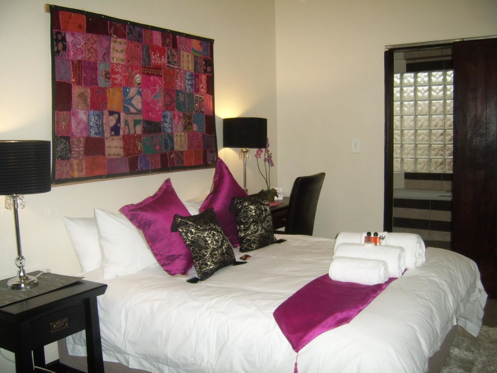 Habitación de hotel con una cama grande, ropa de cama blanca, un colcha de colores, un escritorio con lámpara y una silla.