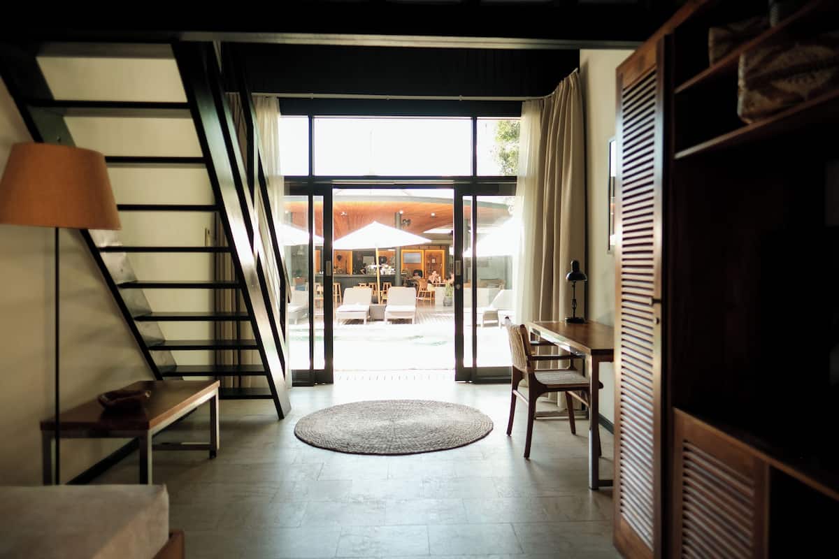 A modern interior with a staircase, a round rug, and a view of an outdoor seating area.