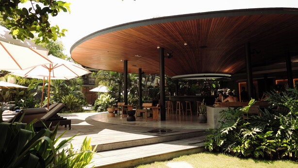 Un espacio lounge moderno al aire libre con suelo de madera, sillones y sombrillas.