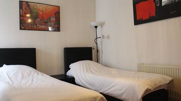 A hotel room with two single beds, a nightstand, a lamp, and a painting on the wall.