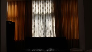 A dimly lit room with a large window covered by sheer curtains, a dark sofa, and a small round table. - MyCityLofts - Schiekade (Rotterdam)