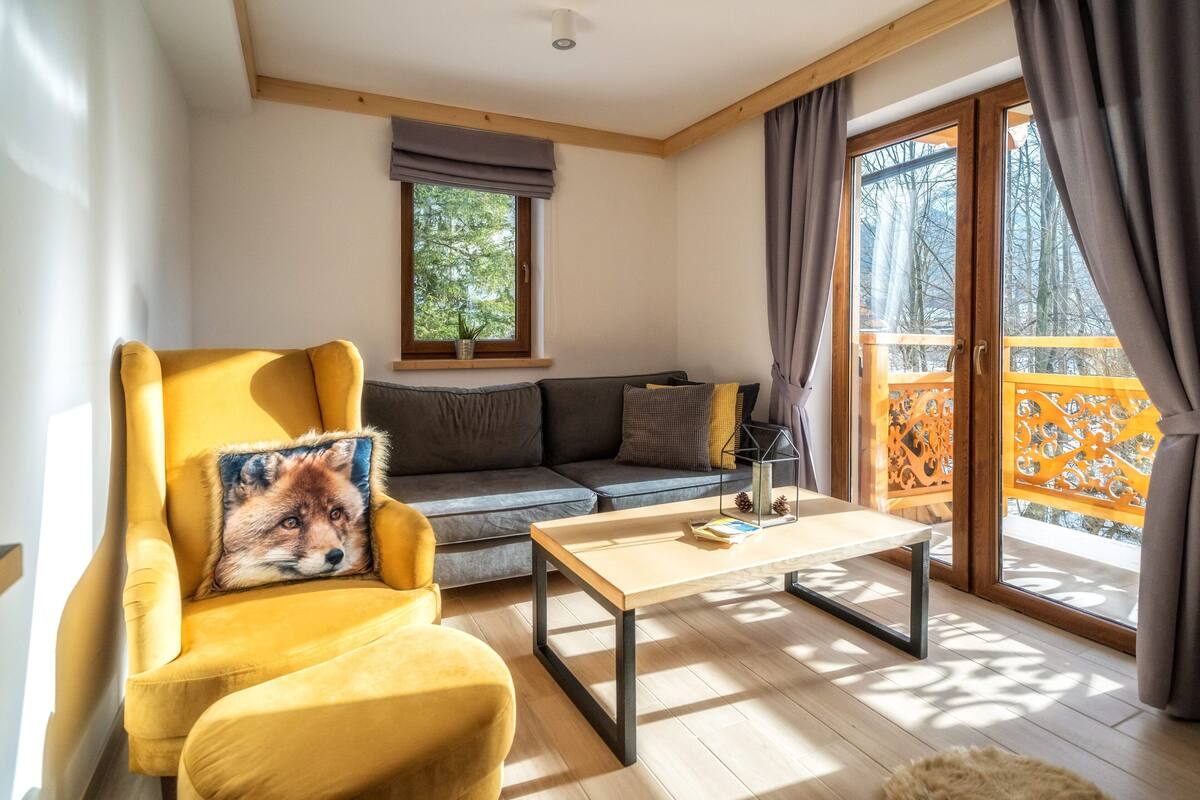 A cozy living room with a yellow armchair, a gray sofa, and a wooden coffee table.