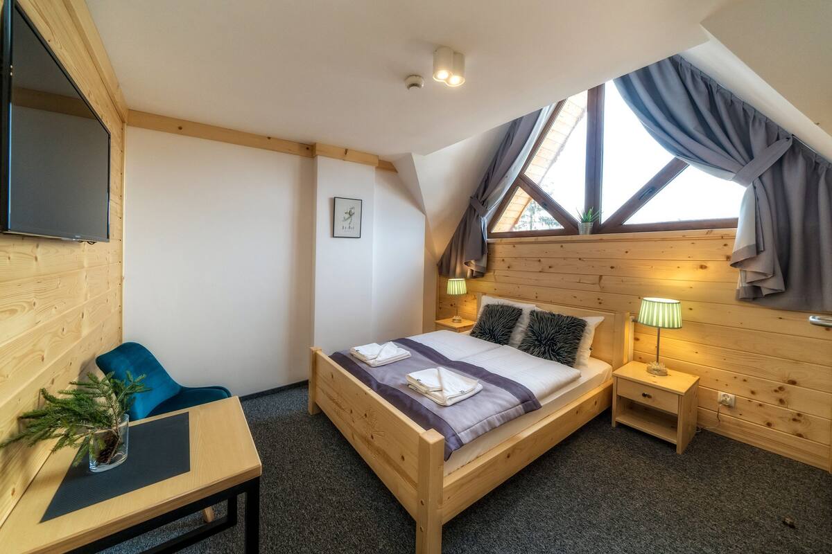 A wooden room with a bed, a desk, and a TV.