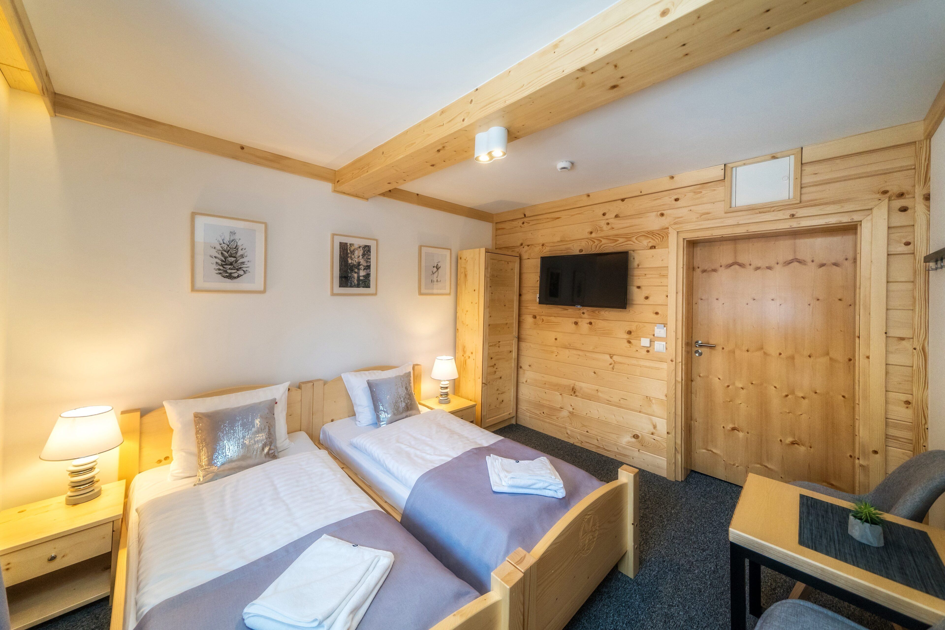 A hotel room with two beds, wooden walls, a TV, and a small table with a chair.